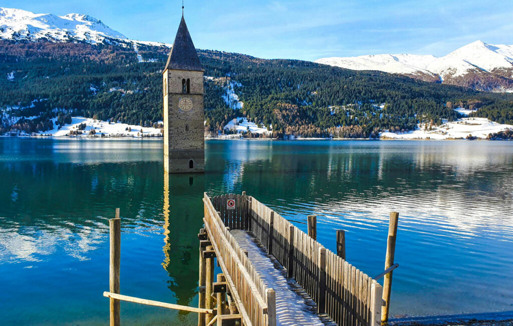 Mountain lake with clock tower and wooden dock in winter scenery.