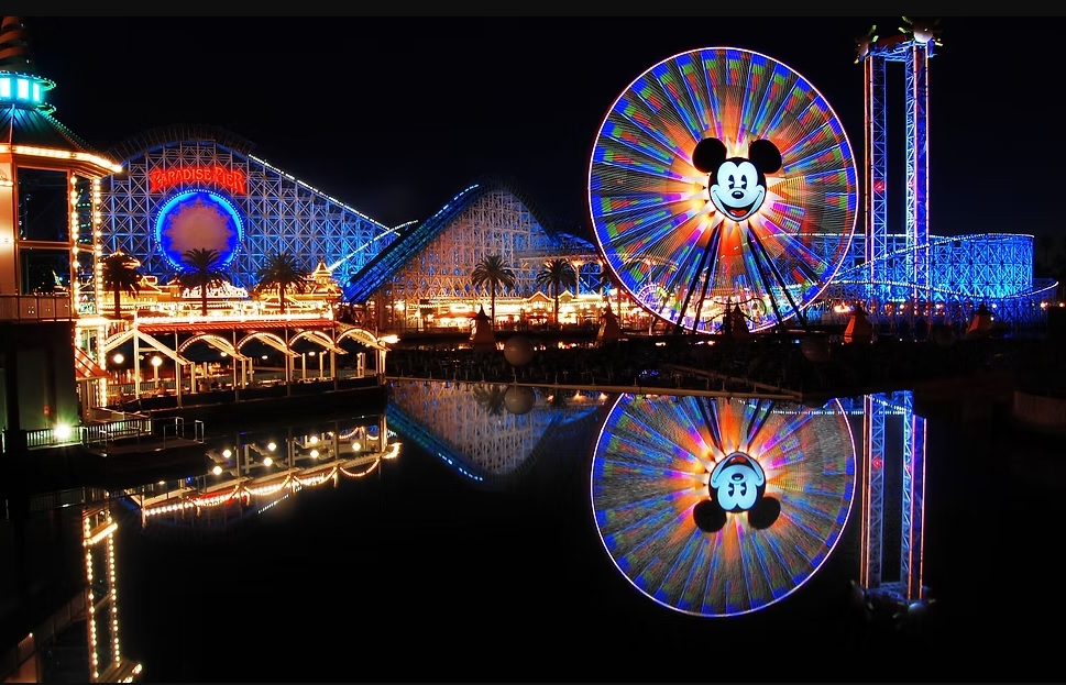 Nighttime amusement park with illuminated ferris wheel and attractions reflected on water.