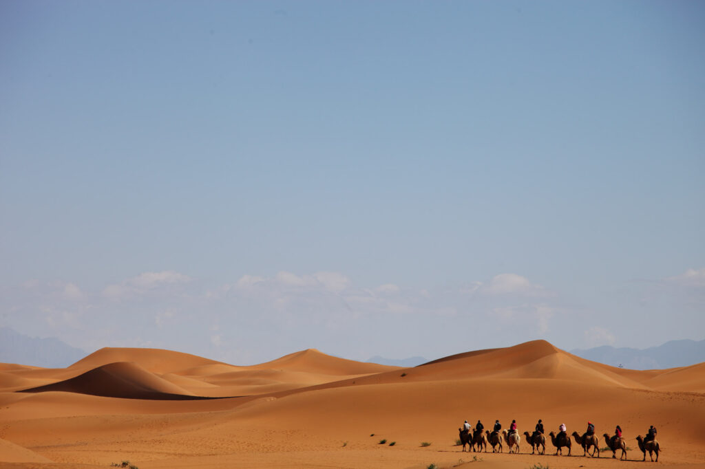Camel caravan traveling across desert sand dunes under open sky.
