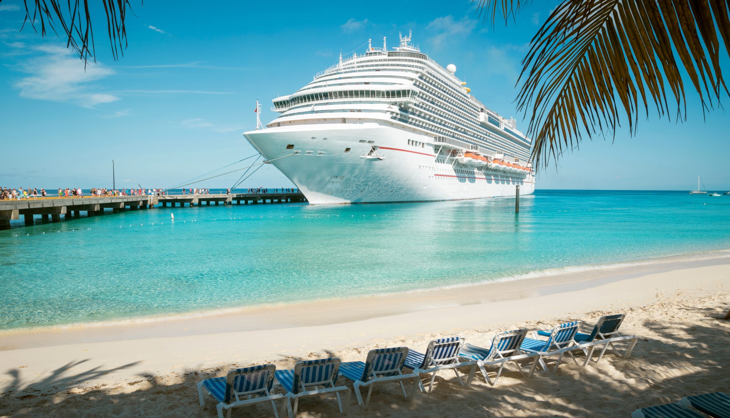 Cruise ship near a calm beach with clear blue water.